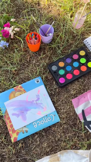 Watercolours, crayons and a painting laid out on the grass
